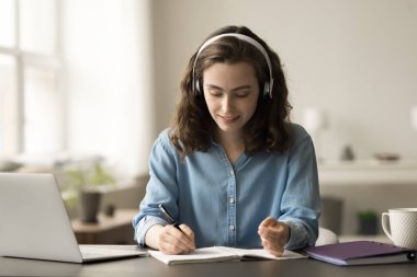 Bilgisayarda özet notlar yazan, çalışma masasında oturan, eğitim konferansını dinleyen, webinar, konferans, konferans ve ses rehberliği öğrenen kulaklıklı, çalışkan bir öğrenci.