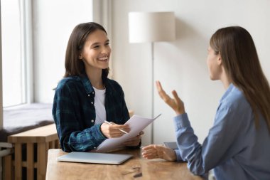 Gayri resmi kıyafet danışmanı iş arkadaşı, elinde kağıt belgeler, çalışma masasında oturan, bayan iş arkadaşıyla konuşan, gülümseyen, gülen,