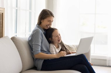 Neşeli anne ve neşeli çocuk komik film izliyor, dizüstü bilgisayarda eğitici karikatür, gülümsüyor, gülüyor, evdeki kanepede dinleniyor, evdeki kablosuz internet iletişiminin keyfini çıkarıyor.