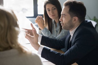 Resmi takım elbiseli kendine güvenen işadamı ofis toplantısında iş arkadaşlarıyla konuşuyor, takım çalışmasını tartışıyor, beyin fırtınası yapıyor, proje üzerinde çalışıyor. Yönetici masadaki iş arkadaşlarıyla konuşuyor.