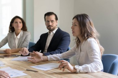 Ciddi genç Asyalı iş kadını ofis toplantısında iş arkadaşlarıyla konuşuyor, konferans masasında konuşuyor, fikirleri açıklıyor, çözümler sunuyor.