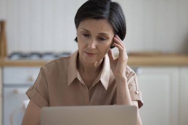 Ev mutfağında dizüstü bilgisayar kullanan, masaya oturan, yüzüne dokunan, ekrana, ekrana bakan, içeriği izleyen, sorunları okuyan, sorunlu,