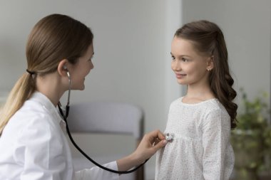 Sağlık kontrolü için çocuk doktorunu ziyaret eden güzel bir kız. Pozitif aile doktoru küçük bir hastayı muayene ediyor, steteskop takıyor, kalp atışlarını dinliyor, nefes alıyor.