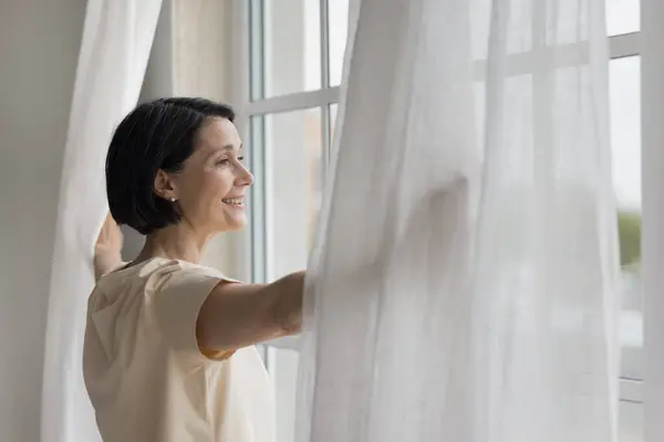 Happy Mature Homeowner Woman Looking Out Big Window Enjoying View Stock-foto