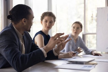 Afrikalı bin yıllık işadamı iş arkadaşlarıyla ofis toplantısında konuşuyor, proje fikrini sunuyor, konuşuyor, pazarlama stratejisini anlatıyor, planı, görevi açıklıyor, iş arkadaşlarıyla çalışma masasında oturuyor.