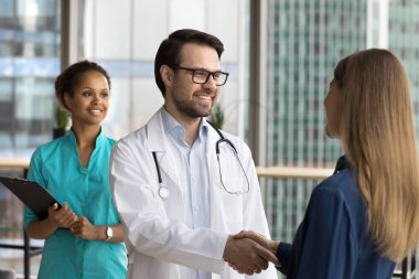 Mutlu yakışıklı doktor adam, minnettar kadın hastayla el sıkışıyor gülümsüyor, gülüyor başarılı terapiyi tartışıyor, tedavi başarısını tartışıyor. Muhtelif tıbbi ekibe danışmanlık için teşekkür eden kadın