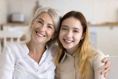 Neşeli, çekici sarışın büyükanne ve güzel ergen çocuk evde portre resmi. Olumlu büyükanne ve çocuk aile toplantısından zevk alıyor, yan yana oturuyor, kameraya bakıyor, sarılıyorlar.