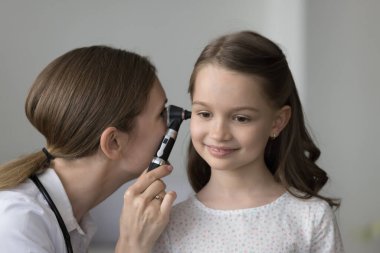 Odaklanmış çocuklar otolarolog kızları kulak enfeksiyonu için muayene ediyor, otoskop kullanıyor. Pozitif, rahat, dost canlısı bir çocuk sağlık kontrolü için doktoru ziyaret ediyor.