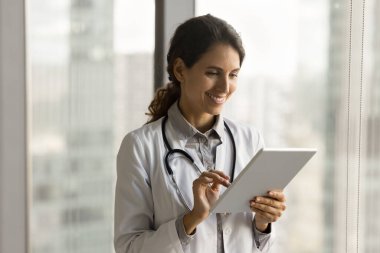 Mutlu, güzel İspanyol doktor kadın online iletişim için tablet kullanıyor, tıbbi konsültasyon, dijital cihaz tutuyor, gülümsüyor. Beyaz üniformalı kadın terapist internette yardım ediyor.