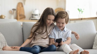 İki meraklı küçük nesil Z çocuğu cep telefonu kullanıyor, evde tek başlarına kanepede oturuyor, arama yapıyor, video oyunu oynuyor, çevrimiçi içerik izliyor, internette geziniyor. Erkek kardeş cep telefonundan kız kardeşe uygulama gösteriyor