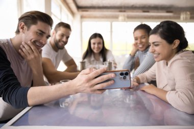 Neşeli çoklu etnik gruptan takım arkadaşları kafede toplanıyor, video görüşmesinde sohbet ediyor, cep telefonu ekranına bakıyor, gülümsüyor, gülüyor. Arkadaşlar grup toplantısını, iletişimi seviyor