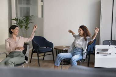 İki neşeli ofis çalışanı kadın işyeri sandalyelerine biniyor, koltuklarda dans ediyor, gülüyor, bağırıyor, şarkı söylüyor, başarıyı kutluyor, eğleniyor, işten keyif alıyor, arkadaşlıktan keyif alıyor.