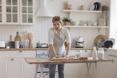 Önlüklü genç ve güzel fırıncı kadın, ev yapımı tatlı, turta, hamur işi, un, yumurta ve ev işleri için fırın yemeği hazırlıyor.