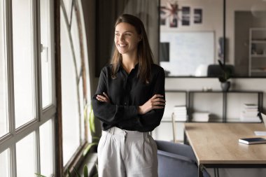 Ofiste elleri çapraz duran, yüzünü çeviren, gülümseyen, gülen, resmi kıyafetli güzel bir yönetici kadın. Mutlu düşünceli kadın iş dünyası profesyonel portre