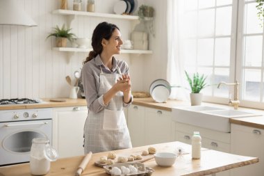 Önlüklü İspanyol kadın mutfakta hamur işleri hazırlar, gülümser, yüzünü çevirir, evde güzel yemekler pişirir, aileye sürpriz yapar, aile tarifi pişirir, ev yapımı çörekler veya hafta sonu evde kurabiyeler pişirir.