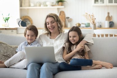 Mutlu anne ve neşeli çocuklar rahat bir evde rahat rahat kanepede dinleniyorlar, film izliyorlar, çizgi film izliyorlar, eğleniyorlar, video konuşmaları yapıyorlar, bilgisayarı internet iletişimi için kullanıyorlar, gülüyorlar.