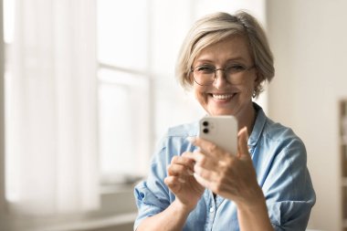 Son sınıf öğrencisi olumlu bir kadın cep telefonundan mesaj yolluyor, selfie çekiyor interneti tarıyor, sosyal medyayı akıllı telefondan arıyor, elinde dişlek tebessümle dijital cihaz tutuyor, gülüyor.