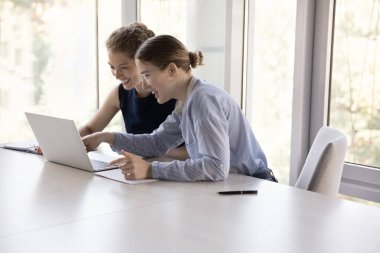 İki neşeli genç bayan çalışan iş yerlerini paylaşıyor, online başvuru kullanıyorlar, internette sunum izliyorlar, gülümsüyorlar, gülüyorlar.