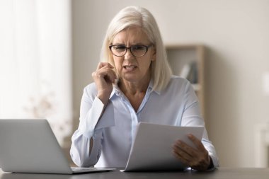 Endişeli yaşlı iş kadını yasal belgeleri okuyor, kızıyor, hata yüzünden hayal kırıklığına uğruyor, yanlış mesaj, anlaşma şartları, finansal kayıplar, dizüstü bilgisayarında evrak işleri yapıyor.