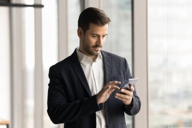 Takım elbiseli ciddi yakışıklı işadamı akıllı telefonda mesaj yazıyor, cep telefonunda internet uygulaması kullanıyor, profesyonel sosyal ağda geziniyor, internet sitesinde geziniyor.