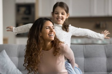 Mutlu bir anne evde heyecanlı güzel bir çocukla aktif oyunlar oynuyor, kızı sırtında taşıyor, çocuğu kolları açık tutuyor, komik anneliğin tadını çıkarıyor, aile oyun zamanı.