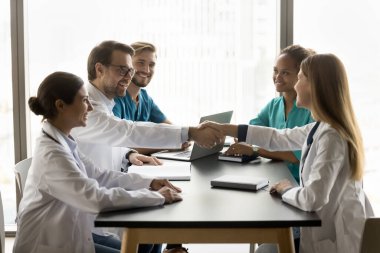 Neşeli genç erkek doktor, tıp seminerinde kadın meslektaşlarıyla el sıkışıyor, işbirliği yapıyor, gülümsüyor, gülüyor, tokalaşıyor. Çeşitli klinik personeli sağlık hizmetlerini tartışıyor