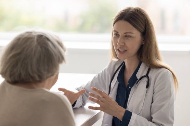 İyimser doktor kadın yaşlı kadın hastayla ofiste buluşuyor, konuşuyor, gülümsüyor, yardım ediyor, danışmanlık yapıyor, yardım ediyor, destek oluyor, sağlık hizmetlerini tartışıyor.
