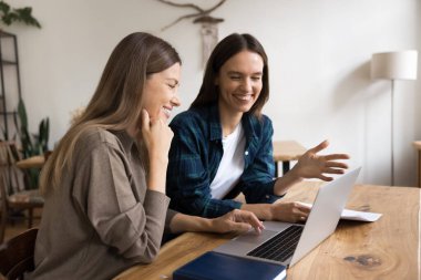 İş yerindeki dizüstü bilgisayarda çalışan neşeli genç iş arkadaşları, gülümsüyor, gülüyor, online medya içeriğini izliyor, internet başlangıç projesini tartışıyorlar.