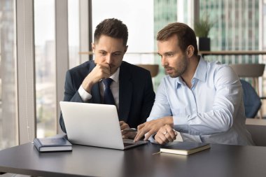 İki ciddi iş arkadaşı iş yerinde dizüstü bilgisayarda birlikte çalışıyor, online başlangıç projesi, strateji, ortaklık, internet girişiminde işbirliği yapıyorlar.