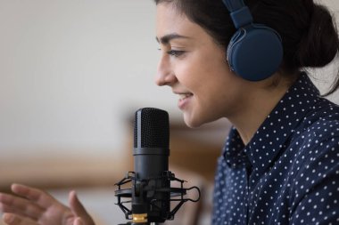 Güzel Hintli radyo DJ 'i, kablosuz kulaklıklı, ses stüdyosu mikrofonunda konuşan, podcast kaydeden, izleyicilerle konuşan mutlu bir kadın. Güzel yüz kenarı görünümü