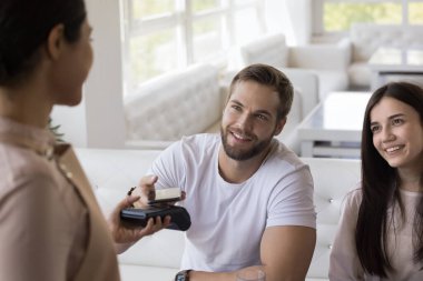 Neşeli bir çift müşteri kafede fatura ödüyor ödeme terminalinde tarama kodunu tarıyor, ticaret perakende satış aletine cep telefonu takıyor, fatura ödüyor, garsona bakıyor, gülümsüyor.