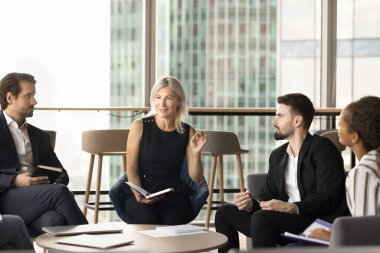 Oldukça olgun bir işletme koçu, ofis personeli eğitimi, konferans veriyor. Ekip lideri kadın, ofiste çalışan çalışanlarla konuşuyor, çeşitli meslektaşlarıyla konuşuyor.