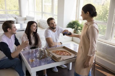Üniformalı sevimli Hintli garson, kafedeki müşteriye POS terminali sunuyor, pizza masasının üzerinde elinde bir cihaz tutuyor. Genç adam, kafeteryada arkadaşlarıyla yemek yiyor, kredi kartı kullanıyor.