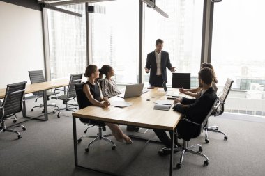 Geniş pencereli, modern şehir içi ofislerinde çeşitli iş adamları toplanıyor, büyük masada oturuyor, konuşuyor, proje üzerinde çalışıyor, beyin fırtınası yapıyor, liderleri dinliyor.