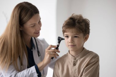 Pozitif odaklı çocuk doktoru çocukların kulaklarını kontrol ediyor, otoskop aleti kullanıyor, gülümsüyor. Hasta çocuk düzenli sağlık muayenesi için aile doktorunu ziyaret ediyor.