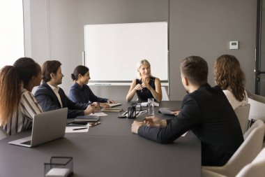 Kendine güvenen orta yaşlı takım lideri kadın çeşitli gruplarla toplantı yapıyor, çalışanlarla konuşuyor, görev, plan, strateji tartışıyorlar. Şirket öğretmeni personele seminer veriyor.