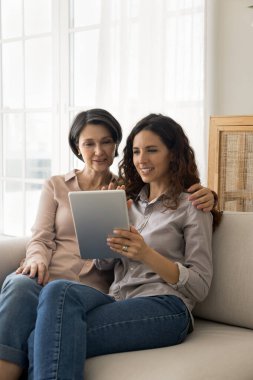 Genç 35 'lik kız ve 60' lık anne tablet kullanıyor, online alışverişleri tartışıyor, ürünleri seçiyor, birlikte elektronik servisler satın alıyorlar. Ticaret müşterileri, pazar uygulaması kullanımı