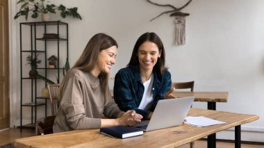 İki neşeli kadın iş ortağı dizüstü bilgisayarda projeyi analiz eden, ofis dairesinde birlikte çalışan, ekrana bakan, gülümseyen, konuşan, internette iletişim için bilgisayarı kullanan kadınlar.