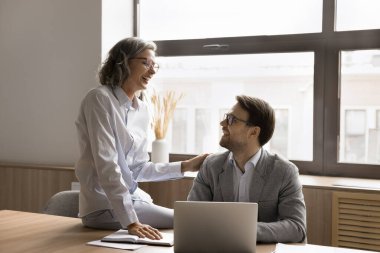 Neşeli iş arkadaşları dizüstü bilgisayarda projeyi tartışıyor, rahatlıyor, gülüyor, eğleniyorlar. Yaşlı profesyonel tavsiye, genç iş arkadaşına destek, dokunaklı omuz