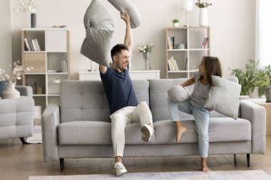 Neşeli baba ve mutlu aktif kız çocuğu rahat oturma odasında yastıklarla kavga ediyorlar, gülüyorlar, oyun oynuyorlar, oyun oynuyorlar, eğleniyorlar.