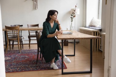 Düşünceli, serbest çalışan bir iş kadını. Küçük bir iş yerinde dijital aletler kullanıyor. Bilgisayarlı masada oturuyor, cep telefonunu tutuyor ve düşünüyor.