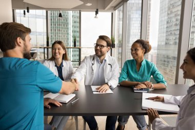 Tıbbi ekip lideri toplantıda cerrahla el sıkışıyor. Zor ve başarılı davaları tartışan mutlu çoklu etnik gruplar, iyi bir iş için uzmanlara el sıkışma imkanı veriyor.