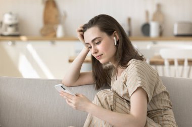 Sakin, yetişkin bir kız akıllı telefon ve kulaklıklarla evde dinleniyor, boş zamanların tadını çıkarıyor, internet iletişimi kuruyor, müzik dinliyor, oyuncuyu açıyor.
