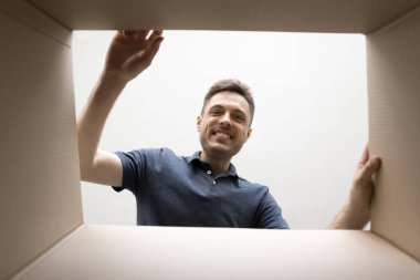 Pozitif genç adam büyük bir karton nakliye kutusu açıyor, içine bakıyor, gülümsüyor, kurye servisinden paketleri açıyor, internet dükkanından sipariş alıyor.