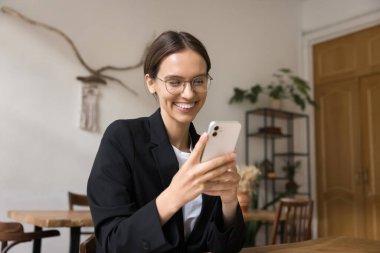 Neşeli genç iş kadını akıllı telefonda online iletişimden, mesajlaşmadan, sohbetten, internetten alışveriş yapmaktan zevk alıyor. Cihazları kullanıyor, modern teknolojiyi başarılı bir iş için kullanıyor.