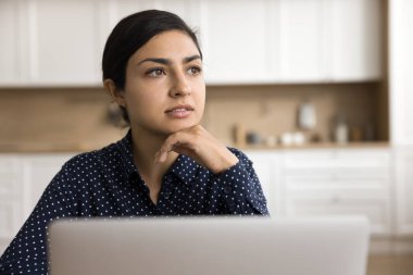 Düşünceli Hintli serbest çalışan kadın dizüstü bilgisayarının başına oturmuş, çenesine dokunuyor, derin düşüncelere dalmış, hayaller kuruyor, karar veriyor, internet teknolojisi, eğitim, iletişim hizmeti hakkında düşünüyor.