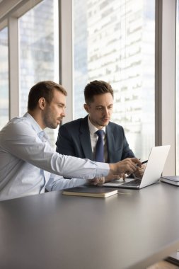 Laptop 'ta çalışan iki ciddi iş adamı, çalışma masasında oturup online proje sunumu izliyorlar, ortaklık, internet girişimi, bilgisayar monitörüne işaret ederek işbirliği yapıyorlar. Dikey çekim