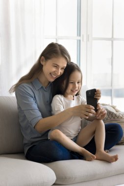 Mutlu, genç bir anne kucağında sevimli bir kız, evde cep telefonu kullanıyor, sevimli küçük kızıyla selfie çekiyor, internetteki internet eğitim uygulamalarıyla çalışmasına yardım ediyor.