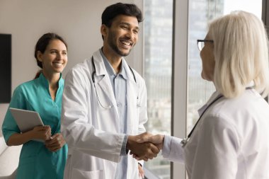 Klinik olgun kafa doktoru genç Hintli stajyeri işe aldığı için tebrik ediyor, sağlık hizmeti alıyor, genç pratisyen erkek ve kadınla el sıkışıyor. Tıp arkadaşları tokalaşıyor.