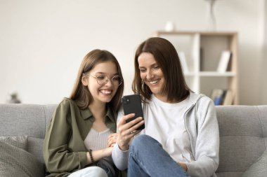 Mutlu anne ve gözlüklü genç çocuk cep telefonunda uygulama kullanıyor, online video görüşmesinde konuşuyor, gülüyor, gülümsüyor, internetten içeriği izliyor.
